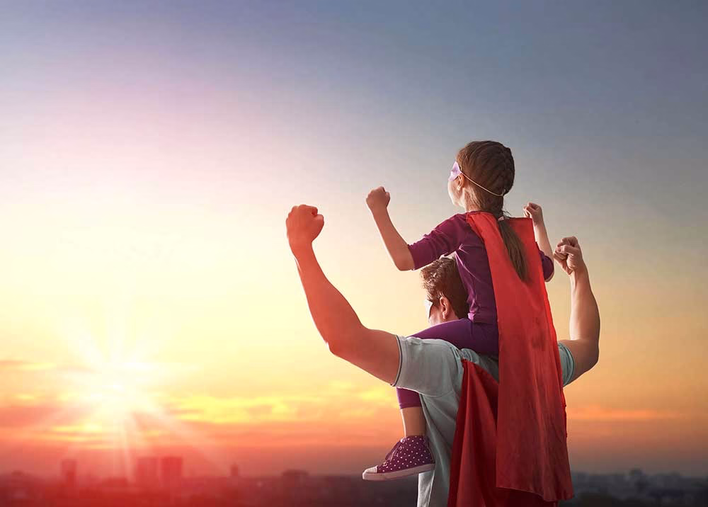 daughter sitting on dad's shoulder wearing capes